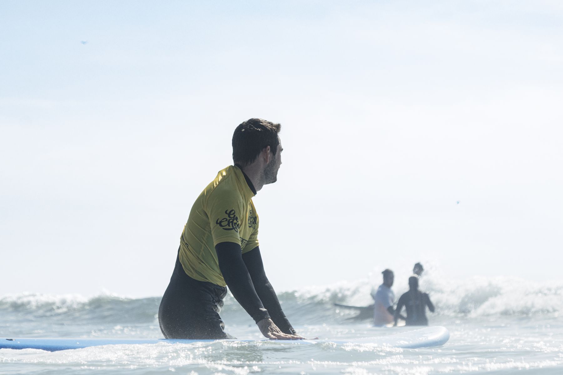 Beginner surfer standing in waist-deep water with a soft board