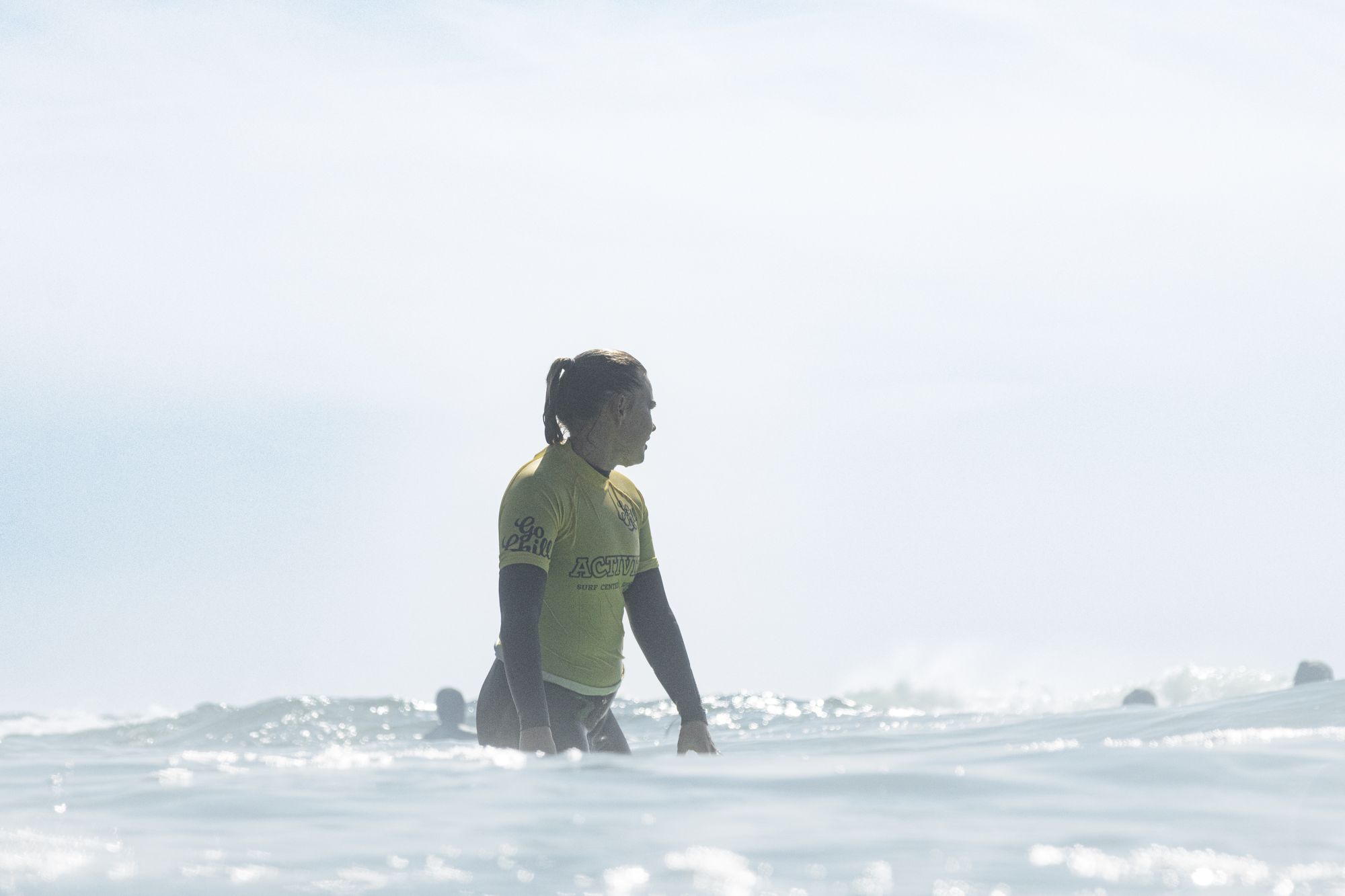 A beginner standing waist-deep in calm water beside a soft surfboard