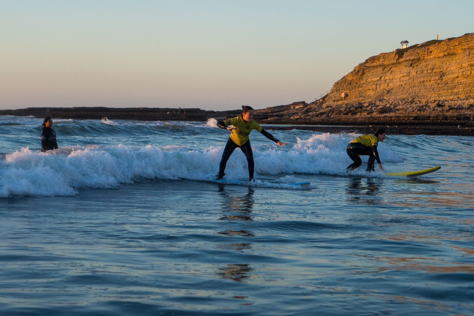 Two friends standing up on soft boards at golden hour, with golden cliffs behind them